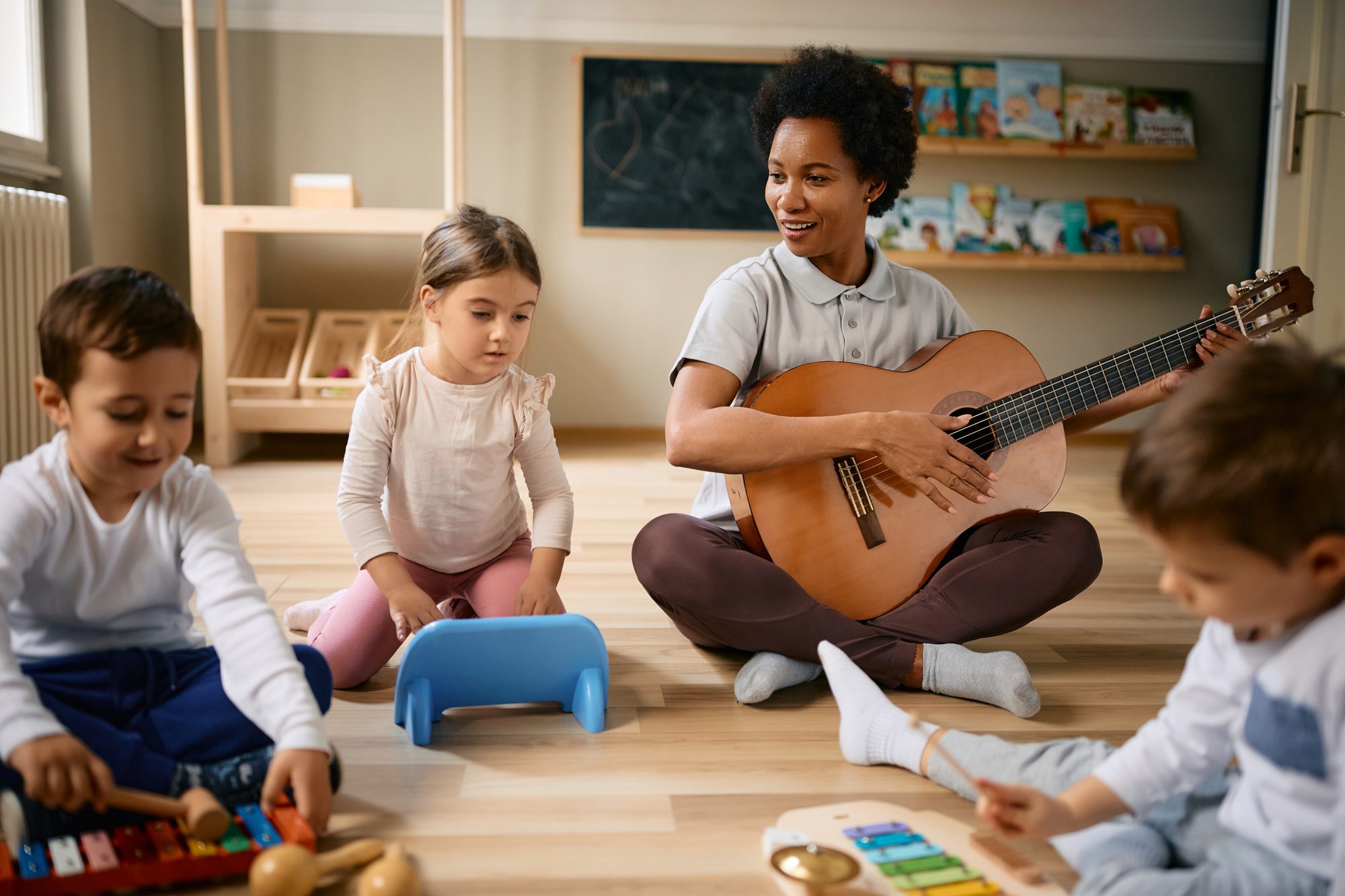 african american teacher and group of kids having fun on music class at kindergarten