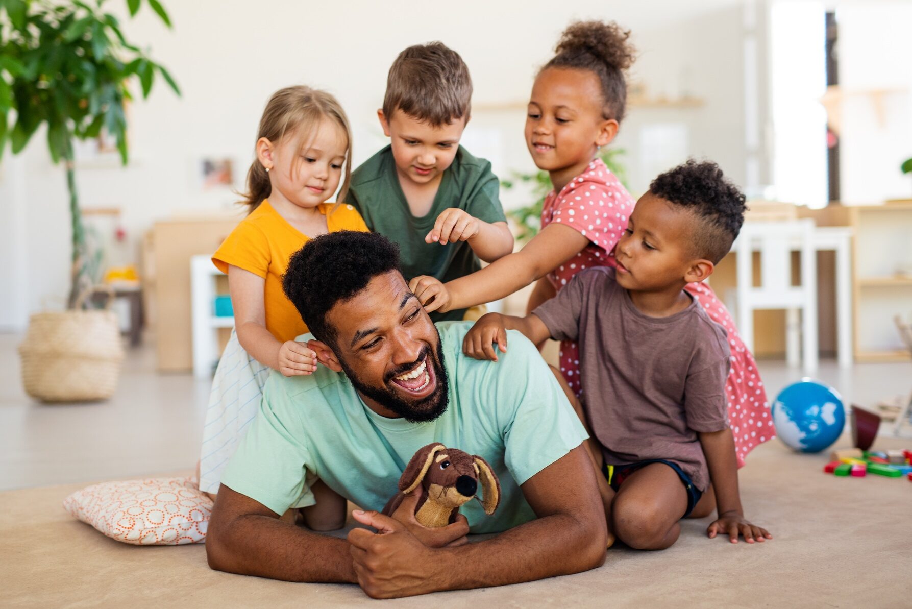 nursery school children with man teacher sitting on floor indoors in classroom playing e1738824469135